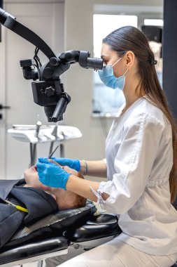 Genç bayan dişçi hastaların dişlerini diş mikroskobuyla tedavi ediyor. Dişçi konsepti. Yüksek kalite fotoğraf. Profesyonel diş tedavisi. Diş ekipmanları.