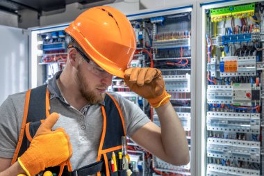 Elektrik panelinde çalışan erkek elektrikçi. Üniformalı erkek elektrikçi. Yüksek kalite fotoğraf. Kasklı ve güvenlik gözlüklü erkek inşaat işçisi..