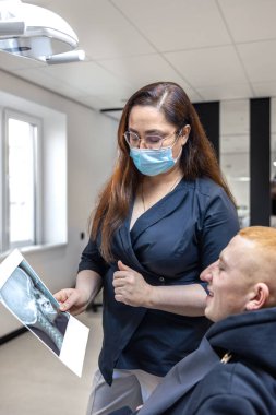 Genç bir dişçi hastaya diş röntgenini gösteriyor. Dişçi konsepti. Yüksek kalite fotoğraf. İşte bir dişçi. Dişçi ve hasta. Bir kadının yüzünde maske.