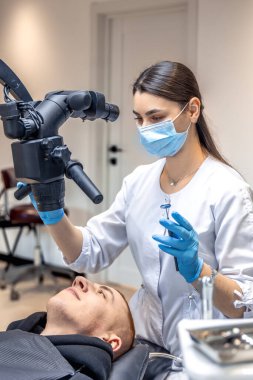 Genç bayan dişçi hastaların dişlerini diş mikroskobuyla tedavi ediyor. Dişçi konsepti. Yüksek kalite fotoğraf. Profesyonel diş tedavisi. Diş ekipmanları.