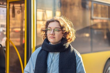 Toplu taşıma. Otobüsü bekliyorum. Öğrenci kız nakil için bekliyor. Yüksek kalite fotoğraf. Gözlüklü ve ceketli kız..