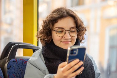 Bir kız öğrenci toplu taşımaya biniyor. Toplu taşıma ve insan konsepti. Yüksek kalite fotoğraf. Bir kız elinde telefonla toplu taşıma aracına biniyor..