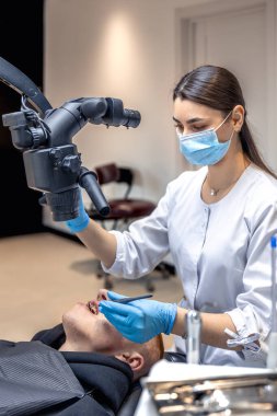 Genç bayan dişçi hastaların dişlerini diş mikroskobuyla tedavi ediyor. Dişçi konsepti. Yüksek kalite fotoğraf. Profesyonel diş tedavisi. Diş ekipmanları.