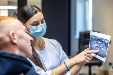 Genç bir dişçi hastaya diş röntgenini gösteriyor. Dişçi konsepti. Yüksek kalite fotoğraf. İşte bir dişçi. Dişçi ve hasta. Bir kadının yüzünde maske.
