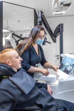 Genç bir dişçi hastaya diş röntgenini gösteriyor. Dişçi konsepti. Yüksek kalite fotoğraf. İşte bir dişçi. Dişçi ve hasta. Bir kadının yüzünde maske.