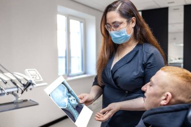 Genç bir dişçi hastaya diş röntgenini gösteriyor. Dişçi konsepti. Yüksek kalite fotoğraf. İşte bir dişçi. Dişçi ve hasta. Bir kadının yüzünde maske.