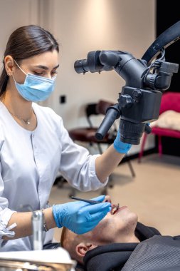 Genç bayan dişçi hastaların dişlerini diş mikroskobuyla tedavi ediyor. Dişçi konsepti. Yüksek kalite fotoğraf. Profesyonel diş tedavisi. Diş ekipmanları.