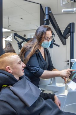 Genç bir dişçi hastaya diş röntgenini gösteriyor. Dişçi konsepti. Yüksek kalite fotoğraf. İşte bir dişçi. Dişçi ve hasta. Bir kadının yüzünde maske.