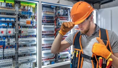Elektrik panelinde çalışan erkek elektrikçi. Üniformalı erkek elektrikçi. Yüksek kalite fotoğraf. Kasklı ve güvenlik gözlüklü erkek inşaat işçisi..