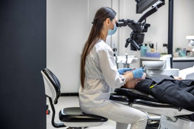 Genç bayan dişçi hastaların dişlerini diş mikroskobuyla tedavi ediyor. Dişçi konsepti. Yüksek kalite fotoğraf. Profesyonel diş tedavisi. Diş aletleri. Boşluğu kopyala.