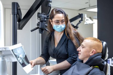 Genç bir dişçi hastaya diş röntgenini gösteriyor. Dişçi konsepti. Yüksek kalite fotoğraf. İşte bir dişçi. Dişçi ve hasta. Bir kadının yüzünde maske.