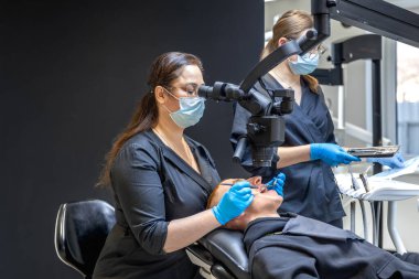 Bir diş hekimi takımı modern ekipmanları kullanarak hastaların dişlerini tedavi eder. Dişçi konsepti. Yüksek kalite fotoğraf. Diş hekimliği ofisinde profesyonel diş tedavisi.