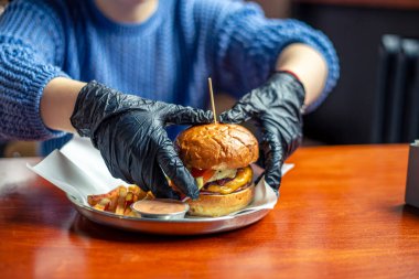 Hamburger tutan bir kadın eli. Fast food. Hile yemeği. Hamburger yakın plan. Yüksek kalite fotoğraf. Fast food konsepti. Eldivenli eller hamburger tutuyor..