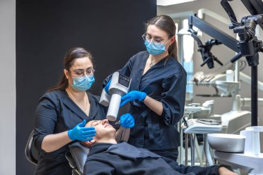 Bir diş hekimi takımı modern ekipmanları kullanarak hastaların dişlerini tedavi eder. Dişçi konsepti. Yüksek kalite fotoğraf. Diş hekimliği ofisinde profesyonel diş tedavisi.