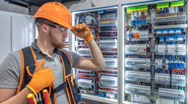Elektrik panelinde çalışan erkek elektrikçi. Üniformalı erkek elektrikçi. Yüksek kalite fotoğraf. Kasklı ve güvenlik gözlüklü erkek inşaat işçisi. Boşluğu kopyala.