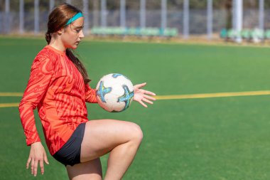 Futbol sahasındaki kız. Futbol antrenmanı. Aktif yaşam tarzı. Futbol konsepti. Yüksek kalite fotoğraf. Mesaj için yer var. Futbol formalı bir kız futbol topuyla oynuyor..