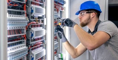 Santralde çalışan üniformalı bir erkek elektrikçi. Elektrik var. Yüksek kalite fotoğraf. Sert şapkalı erkek elektrikçi. Erkek bir elektrikçi elektrikle ilgili bir sorunu çözer.