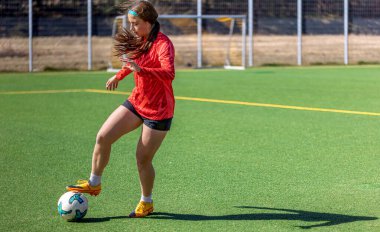 Futbol sahasındaki kız. Futbol antrenmanı. Aktif yaşam tarzı. Futbol konsepti. Yüksek kalite fotoğraf. Mesaj için yer var. Futbol formalı bir kız futbol topuyla oynuyor..
