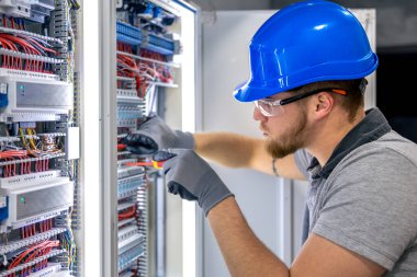 Santralde çalışan üniformalı bir erkek elektrikçi. Elektrik var. Yüksek kalite fotoğraf. Sert şapkalı erkek elektrikçi. Erkek bir elektrikçi elektrikle ilgili bir sorunu çözer.