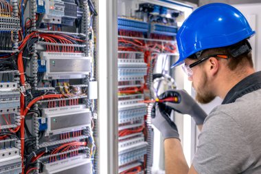 Santralde çalışan üniformalı bir erkek elektrikçi. Elektrik var. Yüksek kalite fotoğraf. Sert şapkalı erkek elektrikçi. Erkek bir elektrikçi elektrikle ilgili bir sorunu çözer.