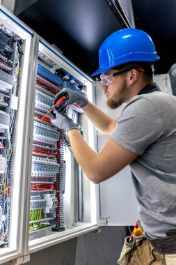 Santralde çalışan üniformalı bir erkek elektrikçi. Elektrik var. Yüksek kalite fotoğraf. Sert şapkalı erkek elektrikçi. Erkek bir elektrikçi elektrikle ilgili bir sorunu çözer.