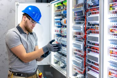 Santralde çalışan üniformalı bir erkek elektrikçi. Elektrik var. Yüksek kalite fotoğraf. Sert şapkalı erkek elektrikçi. Erkek bir elektrikçi elektrikle ilgili bir sorunu çözer.