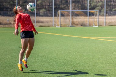 Futbol sahasındaki kız. Futbol antrenmanı. Aktif yaşam tarzı. Futbol konsepti. Yüksek kalite fotoğraf. Mesaj için yer var. Futbol formalı bir kız futbol topuyla oynuyor..