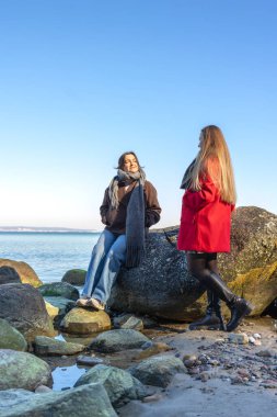 Deniz kıyısında yürüyen iki kadın. İki arkadaş eğleniyor ve birlikte vakit geçiriyorlar. Yüksek kalite fotoğraf. Doğada bir yürüyüş. Boşluğu kopyala.