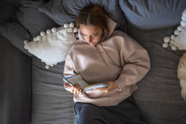 Evde İncil okuyordum. İncil 'i elinde tutan kız. Hıristiyanlık kavramı. Yüksek kalite fotoğraf. Evde İncil okuyorum. Odadaki kanepede oturan genç kız..