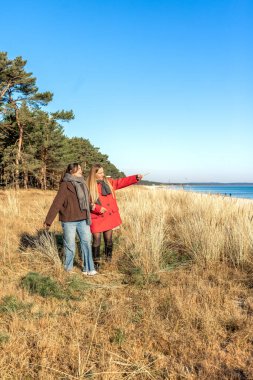 Deniz kıyısında yürüyen iki kadın. İki arkadaş eğleniyor ve birlikte vakit geçiriyorlar. Yüksek kalite fotoğraf. Doğada bir yürüyüş. Uzayı kopyala Soğuk hava.