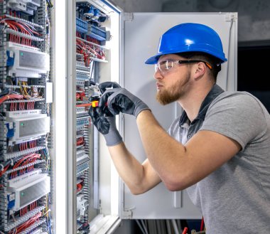 Santralde çalışan üniformalı bir erkek elektrikçi. Elektrik var. Yüksek kalite fotoğraf. Sert şapkalı erkek elektrikçi. Erkek bir elektrikçi elektrikle ilgili bir sorunu çözer.