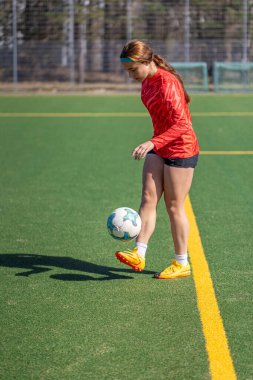 Futbol sahasındaki kız. Futbol antrenmanı. Aktif yaşam tarzı. Futbol konsepti. Yüksek kalite fotoğraf. Futbol formalı bir kız futbol topuyla oynuyor..