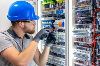 Santralde çalışan üniformalı bir erkek elektrikçi. Elektrik var. Yüksek kalite fotoğraf. Sert şapkalı erkek elektrikçi. Erkek bir elektrikçi elektrikle ilgili bir sorunu çözer.