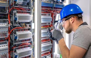 Santralde çalışan üniformalı bir erkek elektrikçi. Elektrik var. Yüksek kalite fotoğraf. Sert şapkalı erkek elektrikçi. Erkek bir elektrikçi elektrikle ilgili bir sorunu çözer.