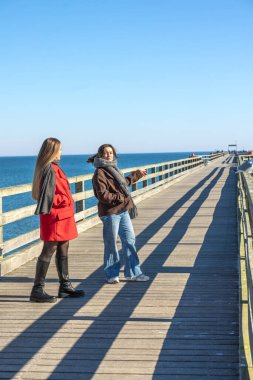 İskelede iki kadın. Rıhtımda yürüyen iki kadın. Yüksek kalite fotoğraf. Deniz. Mesaj için yer var. Gezinti güvertesinde yürü.