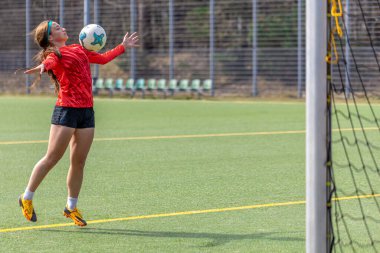 Futbol sahasındaki kız. Futbol antrenmanı. Aktif yaşam tarzı. Futbol konsepti. Yüksek kalite fotoğraf. Mesaj için yer var. Futbol formalı bir kız futbol topuyla oynuyor..