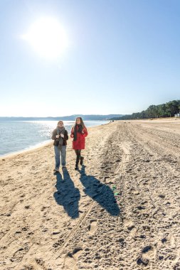 Deniz kıyısında yürüyen iki kadın. İki arkadaş eğleniyor ve birlikte vakit geçiriyorlar. Yüksek kalite fotoğraf. Doğada bir yürüyüş. Uzayı kopyala Soğuk hava.
