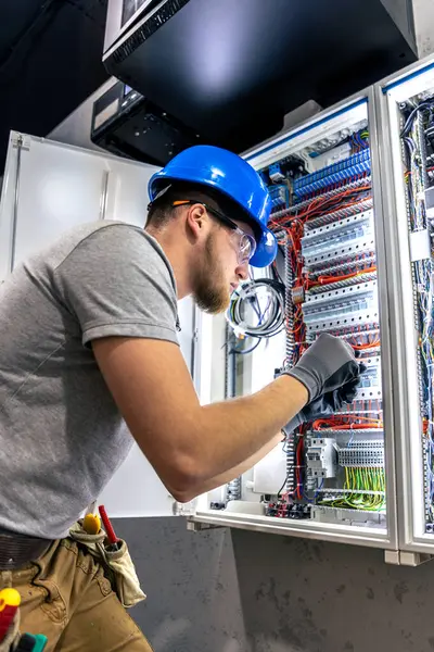 Santralde çalışan üniformalı bir erkek elektrikçi. Elektrik var. Yüksek kalite fotoğraf. Sert şapkalı erkek elektrikçi. Erkek bir elektrikçi elektrikle ilgili bir sorunu çözer.