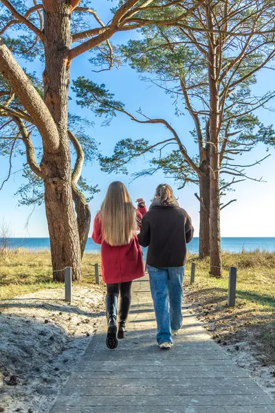 Gezinti güvertesi boyunca yürü. Deniz kenarında bir yürüyüş. Doğada yürümek. Yüksek kalite fotoğraf. Sur boyunca yürüyen iki kadın. Soğuk hava. İki kadın denize doğru yürüyor..