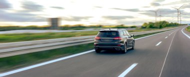 Karanlık bir araba otoban boyunca hareket eder dramatik bir günbatımı gökyüzü altında, özgürlük ve hareket çağrıştırır..