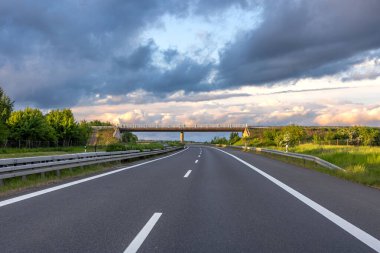 Günbatımında dramatik bir gökyüzü altında köprüsü olan modern bir otoyolun geniş görüşü..