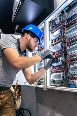 Santralde çalışan üniformalı bir erkek elektrikçi. Elektrik var. Yüksek kalite fotoğraf. Sert şapkalı erkek elektrikçi. Erkek bir elektrikçi elektrikle ilgili bir sorunu çözer.