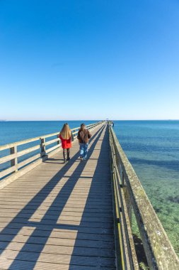 İskelede iki kadın. İskelede yürüyen iki kadının arka görüntüsü. Yüksek kalite fotoğraf. Deniz. Mesaj için yer var. Gezinti güvertesinde yürü.