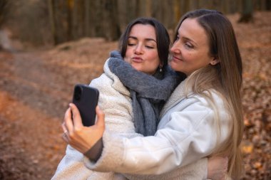 Ormanda telefonlarıyla selfie çeken iki arkadaş. Doğadaki arkadaşlar. Yüksek kalite fotoğraf. İlkbahar, sonbahar mevsimi. Ormanda bir yürüyüş, doğada..