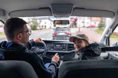 Ön koltukta gülümseyen bir kız kameraya bakarken bir adam şehir caddesinde araba sürüyor. Sıcak ışıklandırma ve rahat atmosfer.