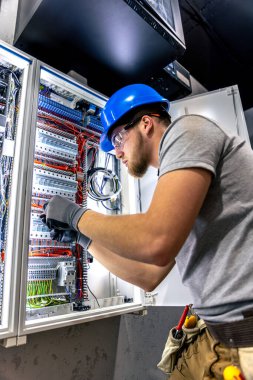 Santralde çalışan üniformalı bir erkek elektrikçi. Elektrik var. Yüksek kalite fotoğraf. Sert şapkalı erkek elektrikçi. Erkek bir elektrikçi elektrikle ilgili bir sorunu çözer.