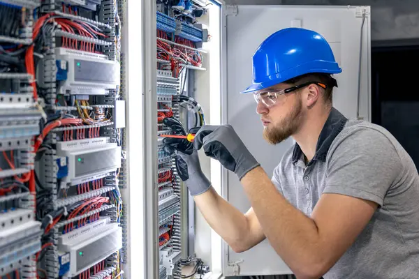 Santralde çalışan üniformalı bir erkek elektrikçi. Elektrik var. Yüksek kalite fotoğraf. Sert şapkalı erkek elektrikçi. Erkek bir elektrikçi elektrikle ilgili bir sorunu çözer.
