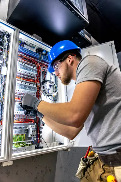 Santralde çalışan üniformalı bir erkek elektrikçi. Elektrik var. Yüksek kalite fotoğraf. Sert şapkalı erkek elektrikçi. Erkek bir elektrikçi elektrikle ilgili bir sorunu çözer.
