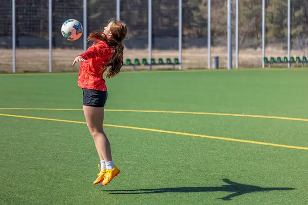 Futbol sahasındaki kız. Futbol antrenmanı. Aktif yaşam tarzı. Futbol konsepti. Yüksek kalite fotoğraf. Mesaj için yer var. Futbol formalı bir kız futbol topuyla oynuyor..