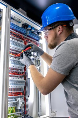 Santralde çalışan üniformalı bir erkek elektrikçi. Elektrik var. Yüksek kalite fotoğraf. Sert şapkalı erkek elektrikçi. Erkek bir elektrikçi elektrikle ilgili bir sorunu çözer.